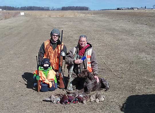 Three generations of hunters, grandfather son & grandson, kneeling for a portrait of themselves and the game birds they have caught.